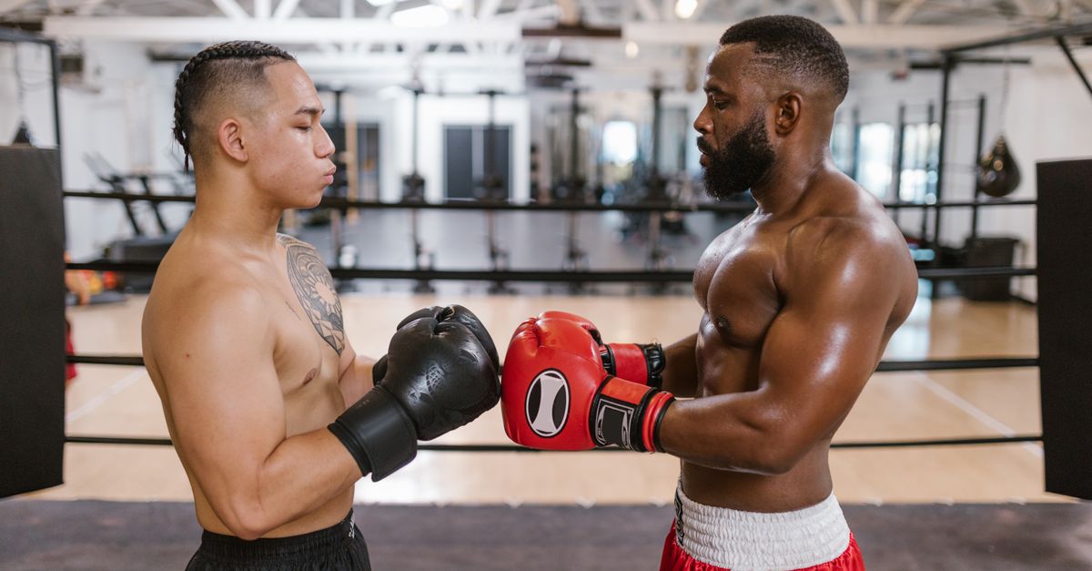 Two shirtless boxers prepare for a match in a gym, highlighting athleticism.